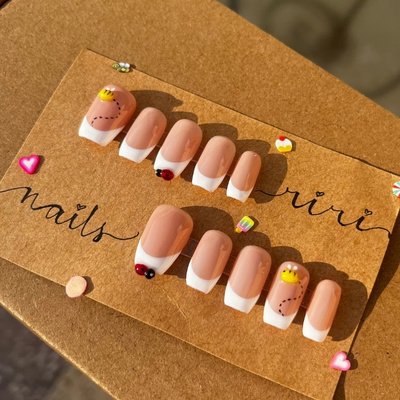 Skin tone French tip press-on nails with black and red bug nail art design displayed on Riri Nails packaging in Muscat, Oman